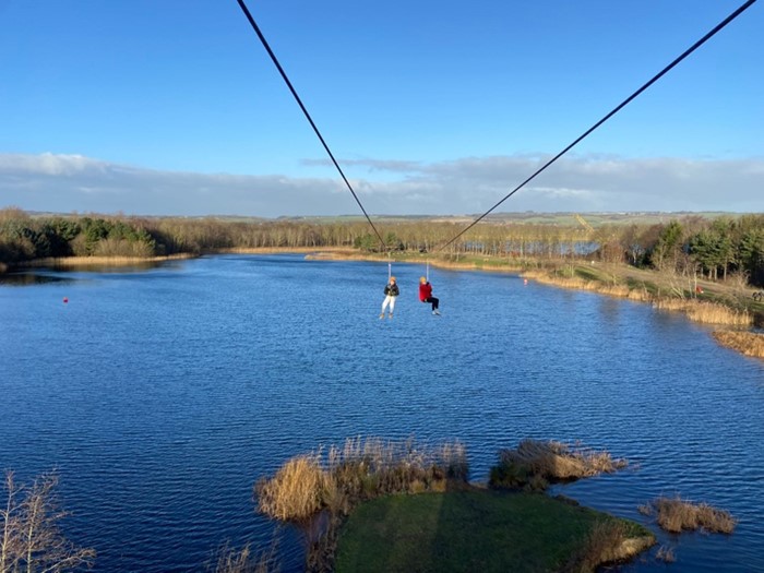 Two people on a zipline, over a lake. 